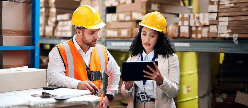 2 people discussing work in a warehouse wearing hard hats